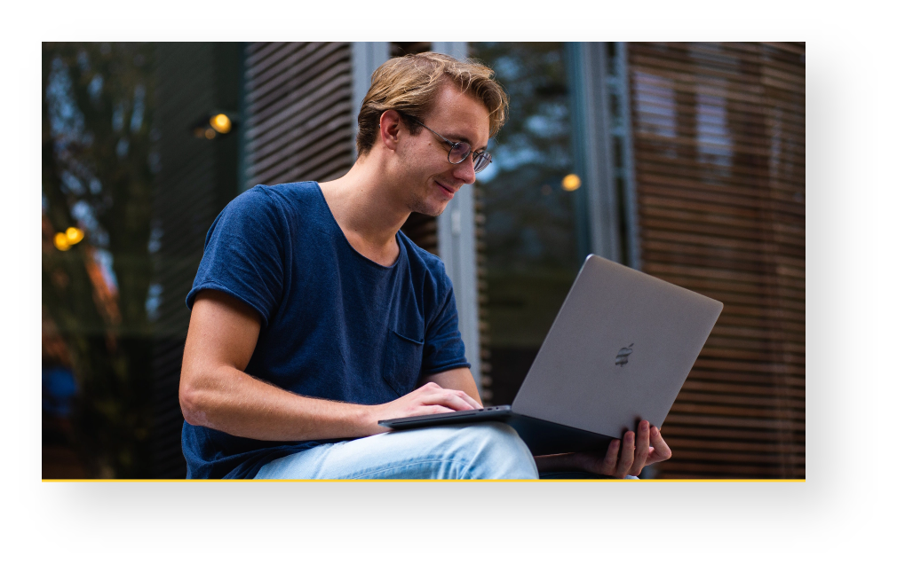 A man with glasses, outside on his laptop